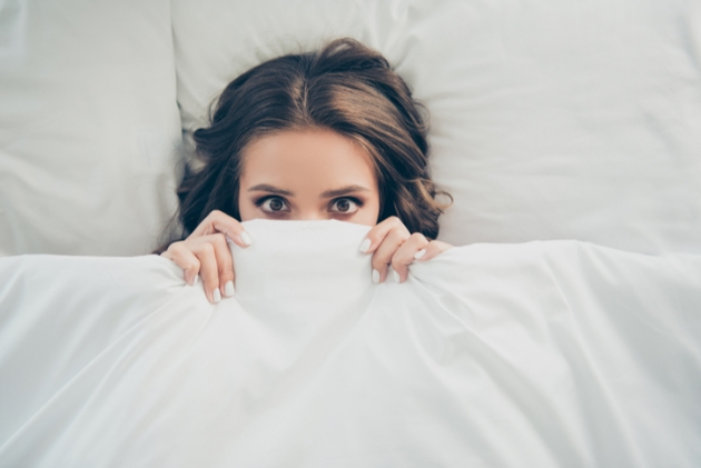 Lady with brown hair hides peaks out from under a duvet