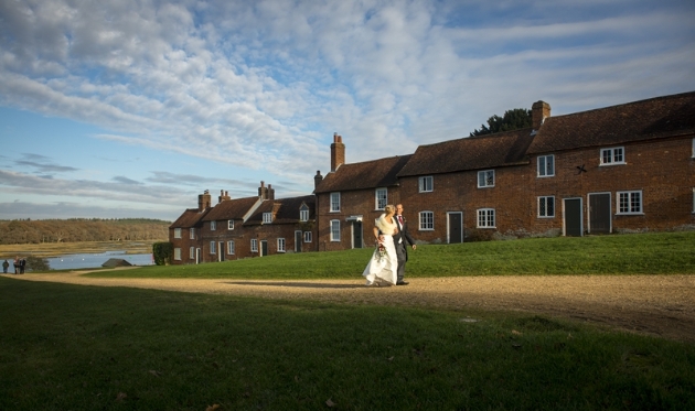 bride and groom walking along path from lake with house running alongside