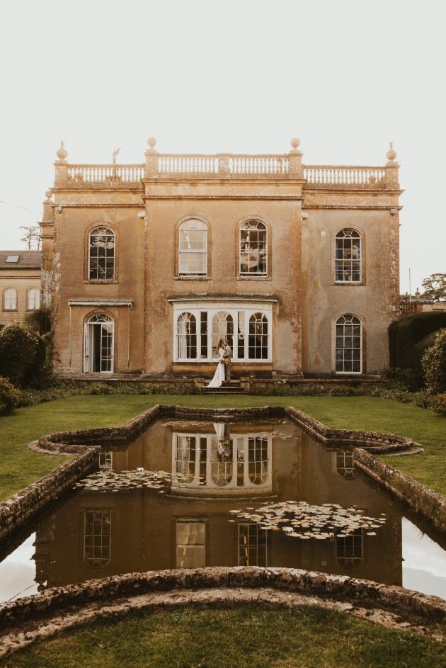 Leweston, Dorset, pale brick house with victorian pond in garden and wedding couple standing on steps of house 