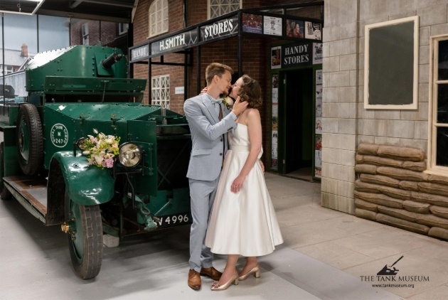 couple in wedding outfits standing in front of vintage vehicle 