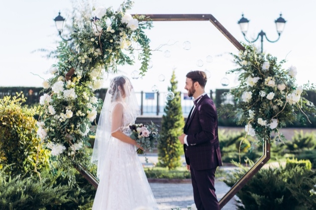 couple tying knot in front of arch outside