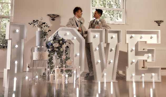 The two grooms standing behind their illuinated love letters