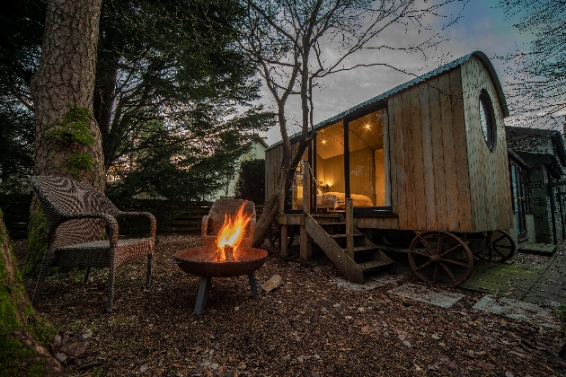 sheperds hut at night with two chairs and firepit outside