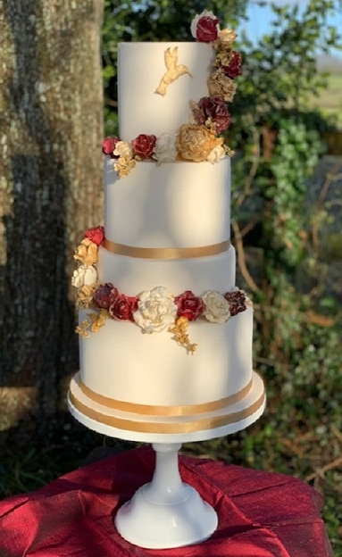 four tier cream cake with red and gold flowers on it 