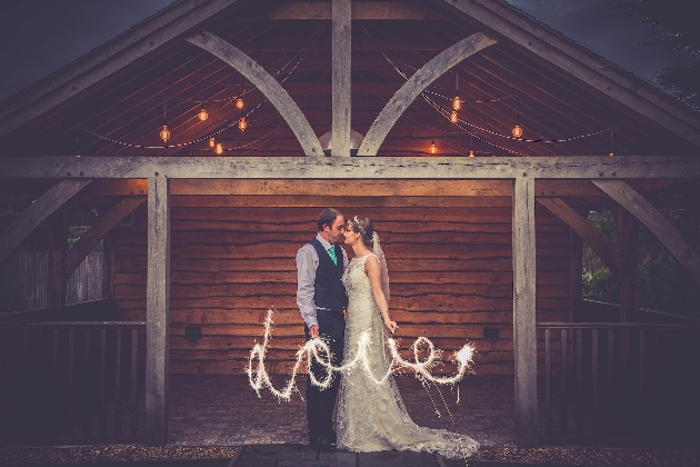 couple at night in wedding gear with sparklers outside barn