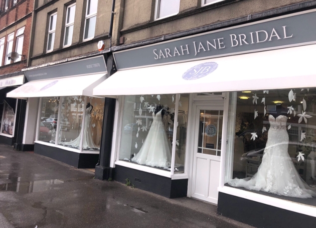 front of bridal boutique shop wth dresses in the window and grey and pink sign