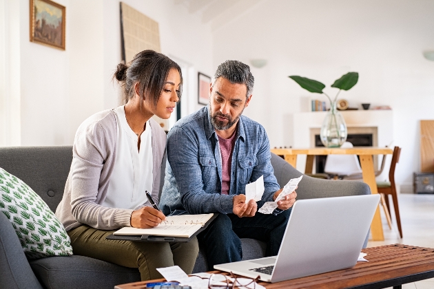 couple on sofa looking through bills at a lap top