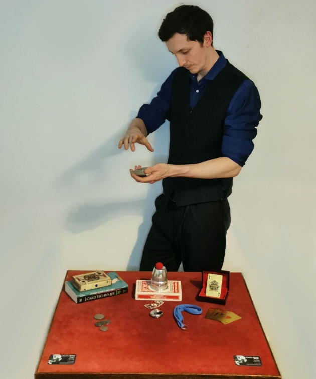 a magician doing a trick stood behind a table of tricks