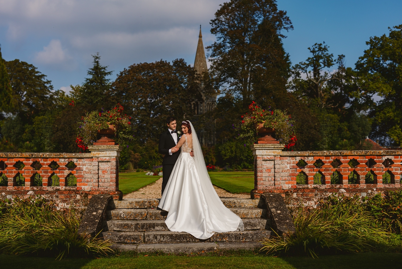 bride and groom stand on red brick steps in formal gardens on sunny day