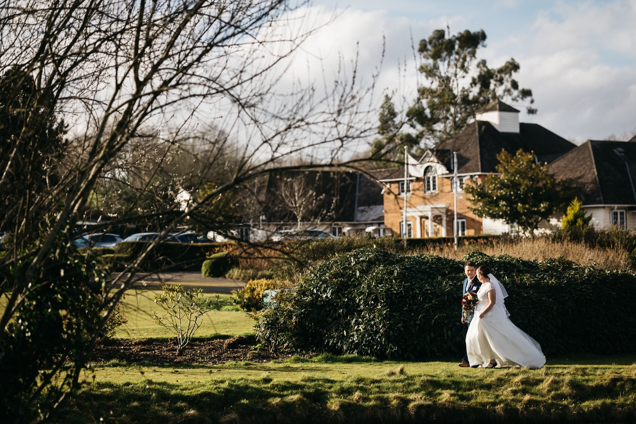 bride and groom on winter's day walking across a golf course