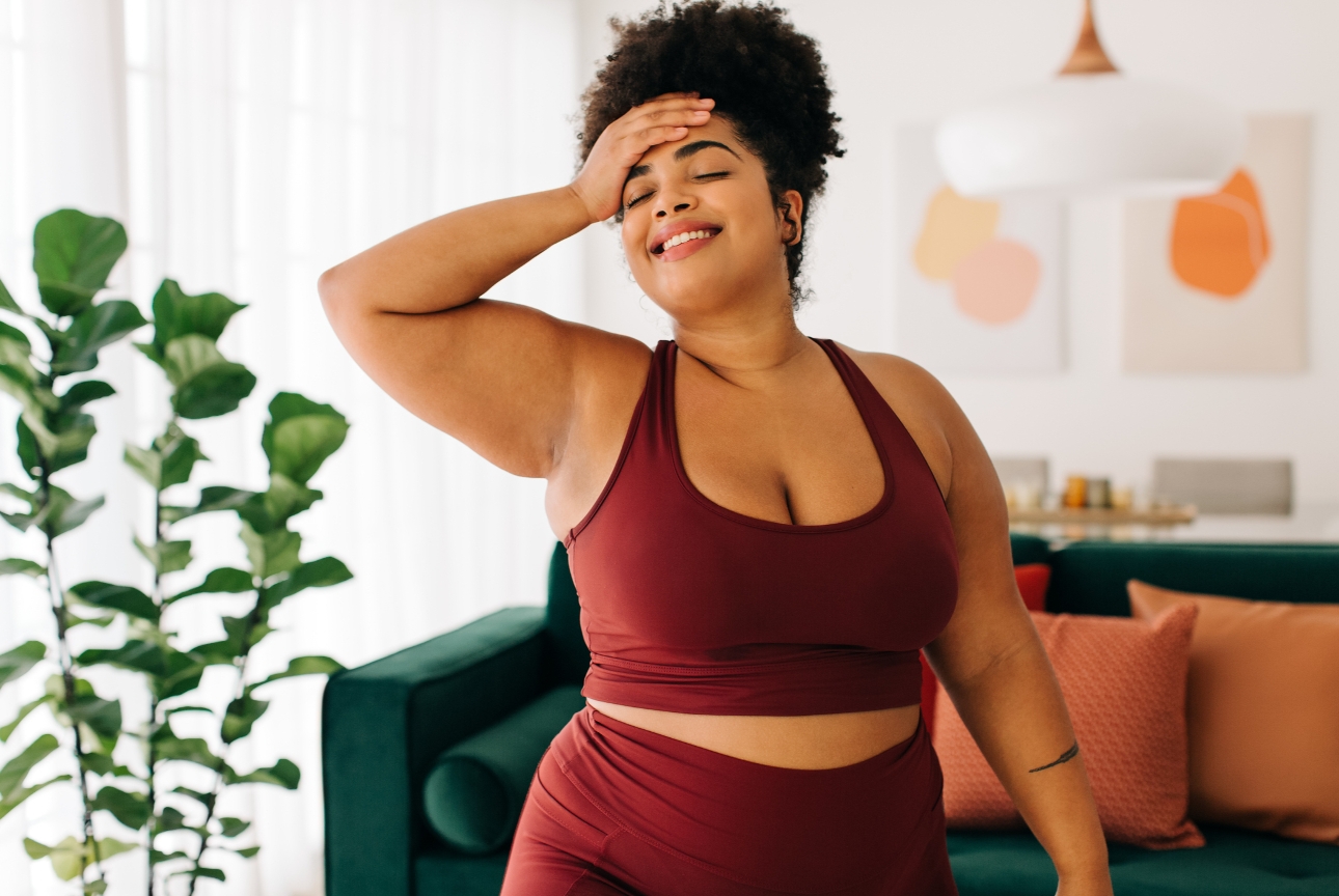 woman in workout gear standing in her lounge with a hand on her head