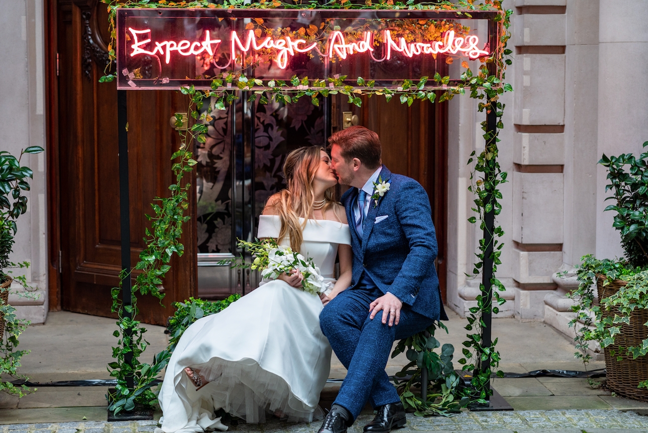 couple sat on chair with retro light around them and flower wall