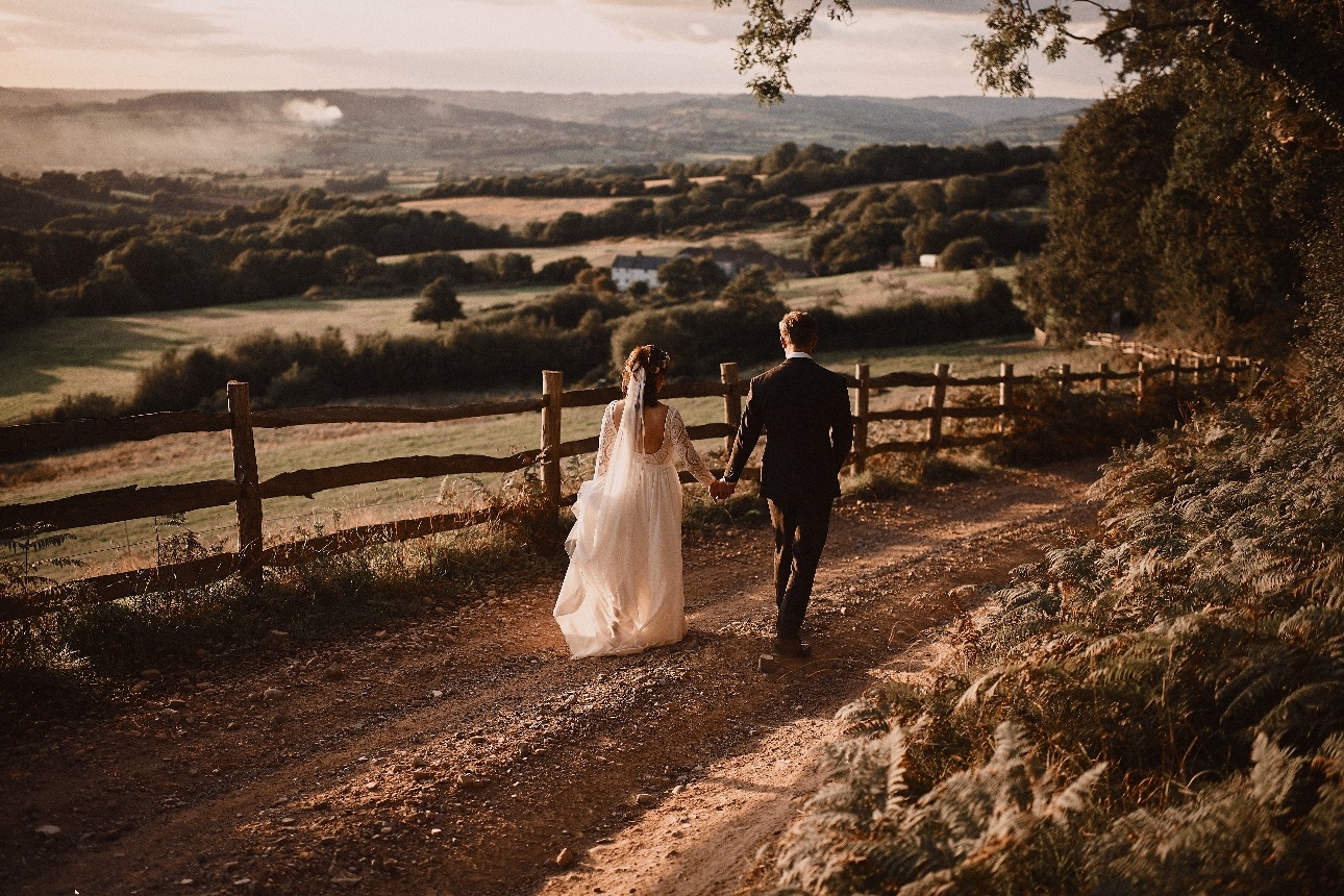 wedding couple walking down a country track with field in the horizon