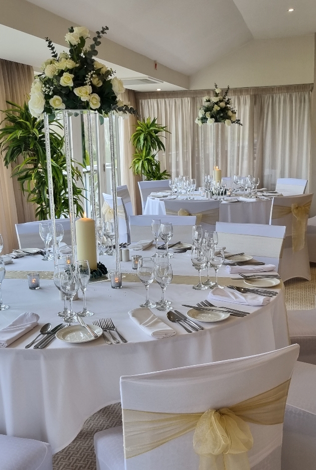 wedding breakfast table set up with white linen and green sash flowers for centrepiece
