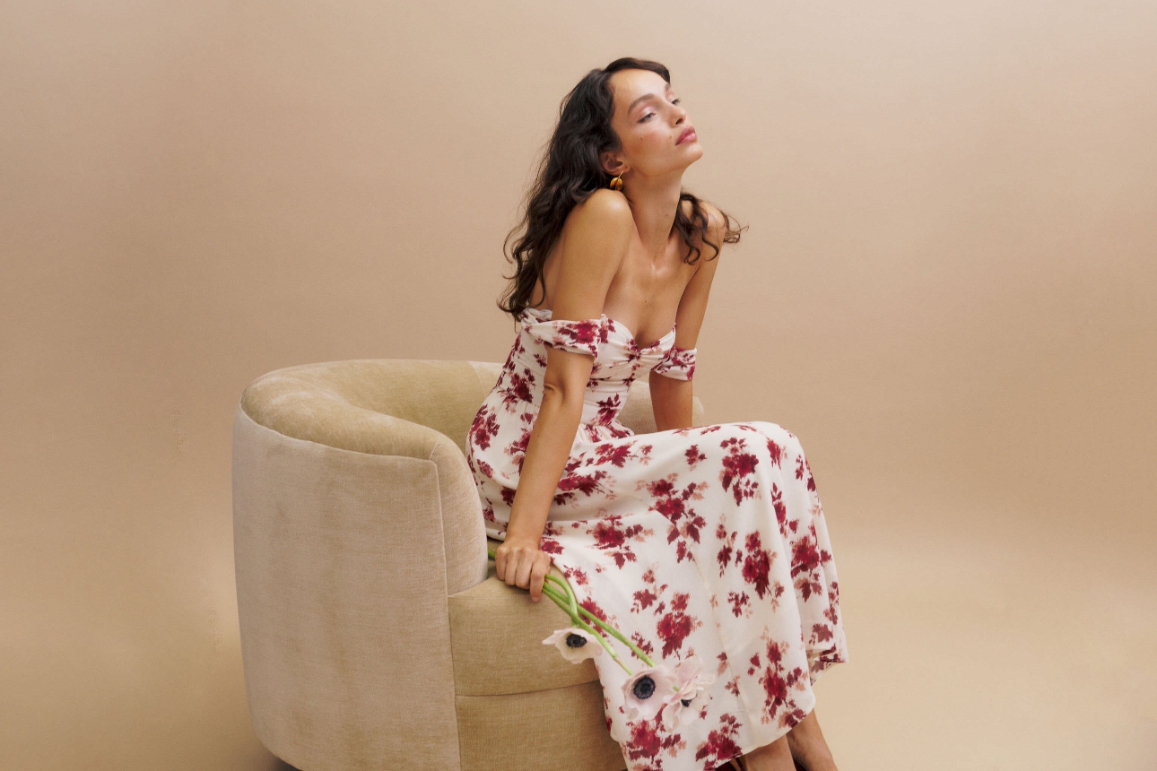 woman sat down on chair in white dress with red flowers on