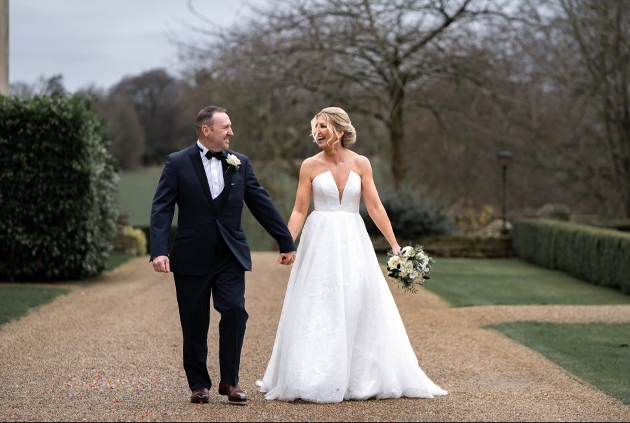 couple in modern wedding attire walking down a gravel path at a show