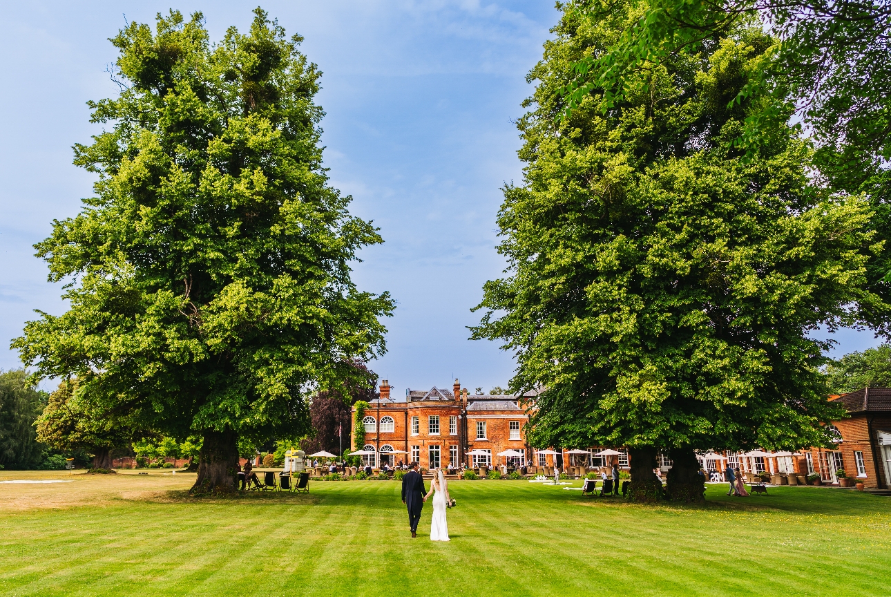 Royal Berkshire hotel, with huge lawn, tall trees, and couple walking from camera towards building