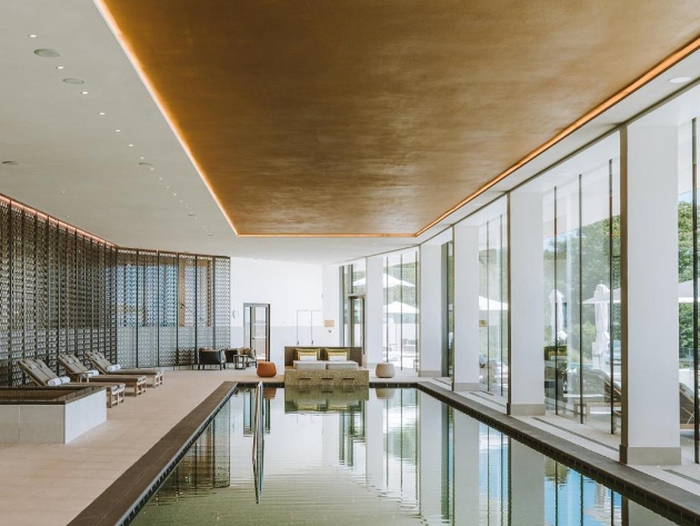 An indoor swimming pool with seats next to it and glass windows