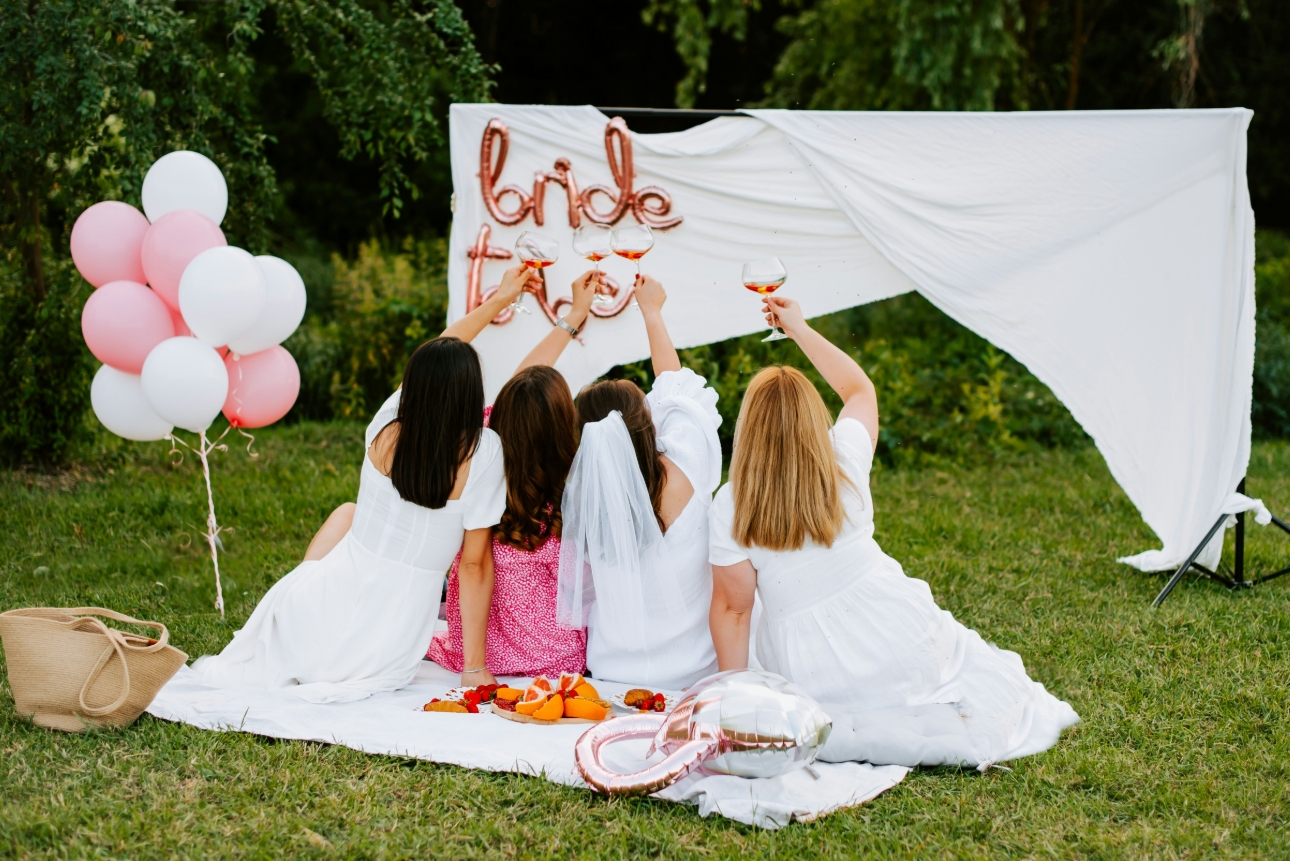 group of friends on ground cheering glass and looking at bride to be banner 